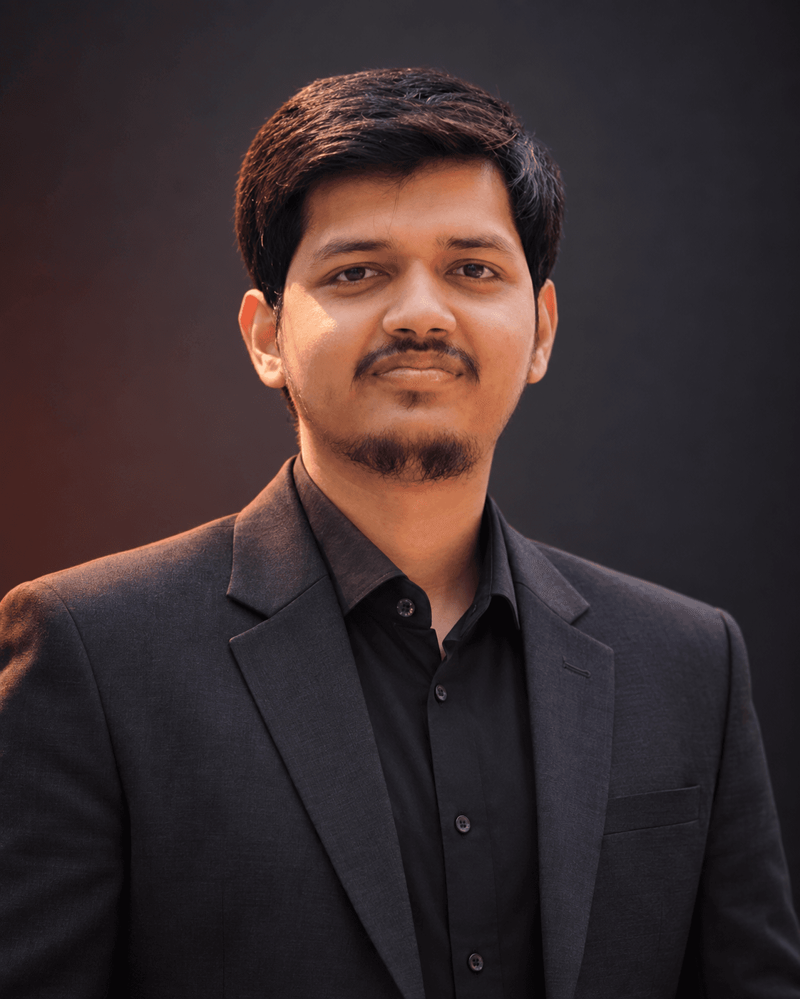 Portrait of Jisan Nuren Siam in a charcoal suit and dark shirt against a dark background.